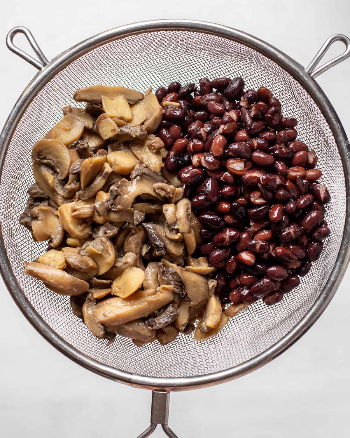 Rinsed canned mushrooms and black beans in a fine-mesh sieve.