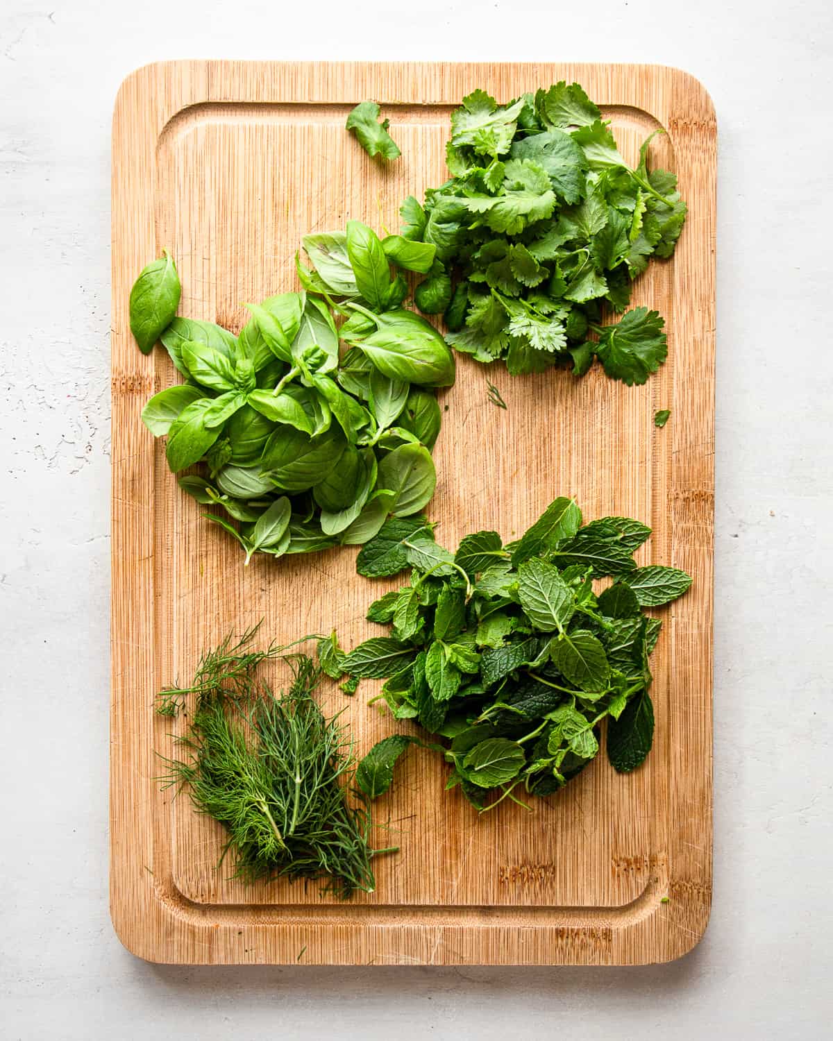 Fresh basil, cilantro, mint, and dill on a wooden cutting board.