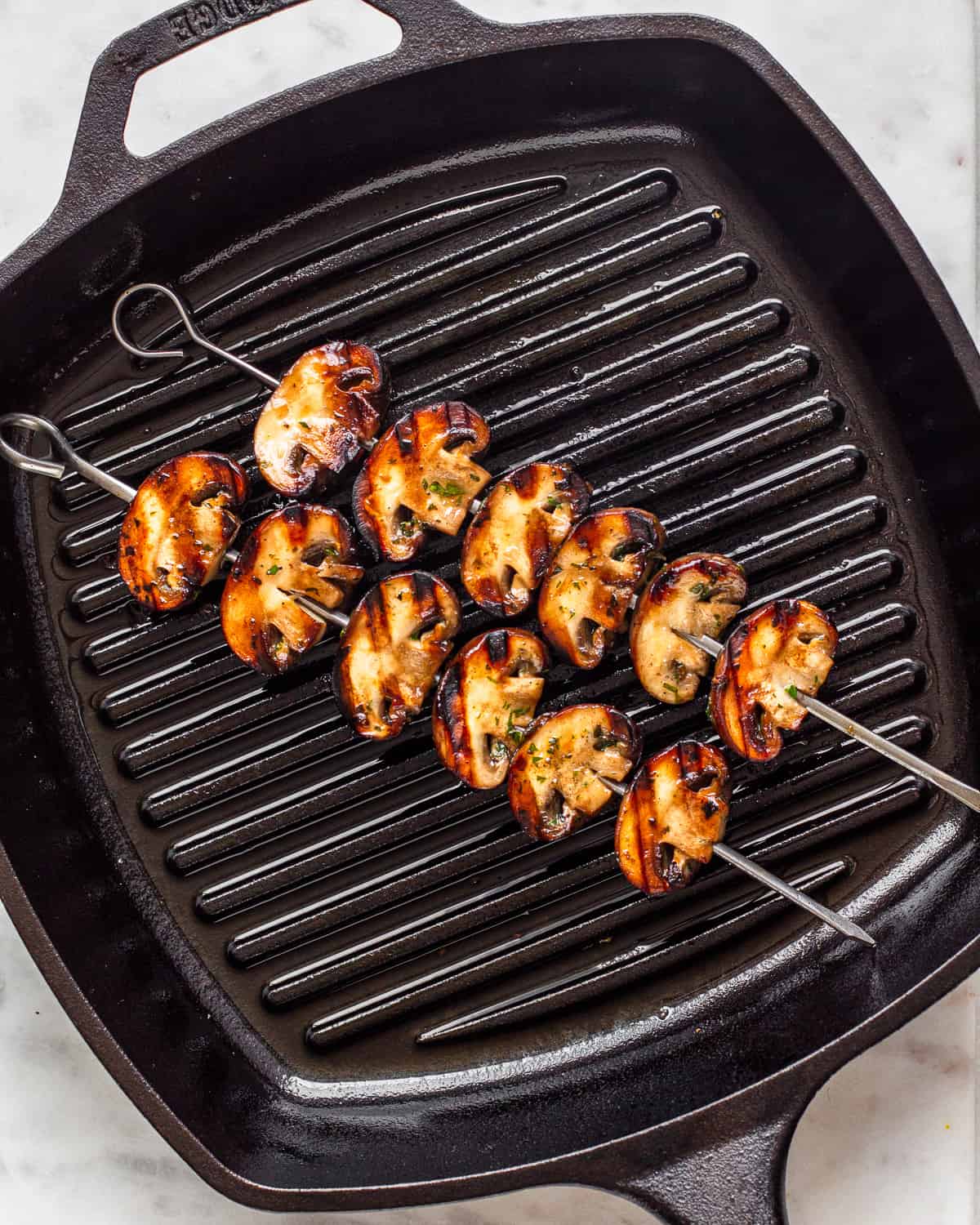 Two mushroom skewers with grill marks in a black cast iron grill pan.