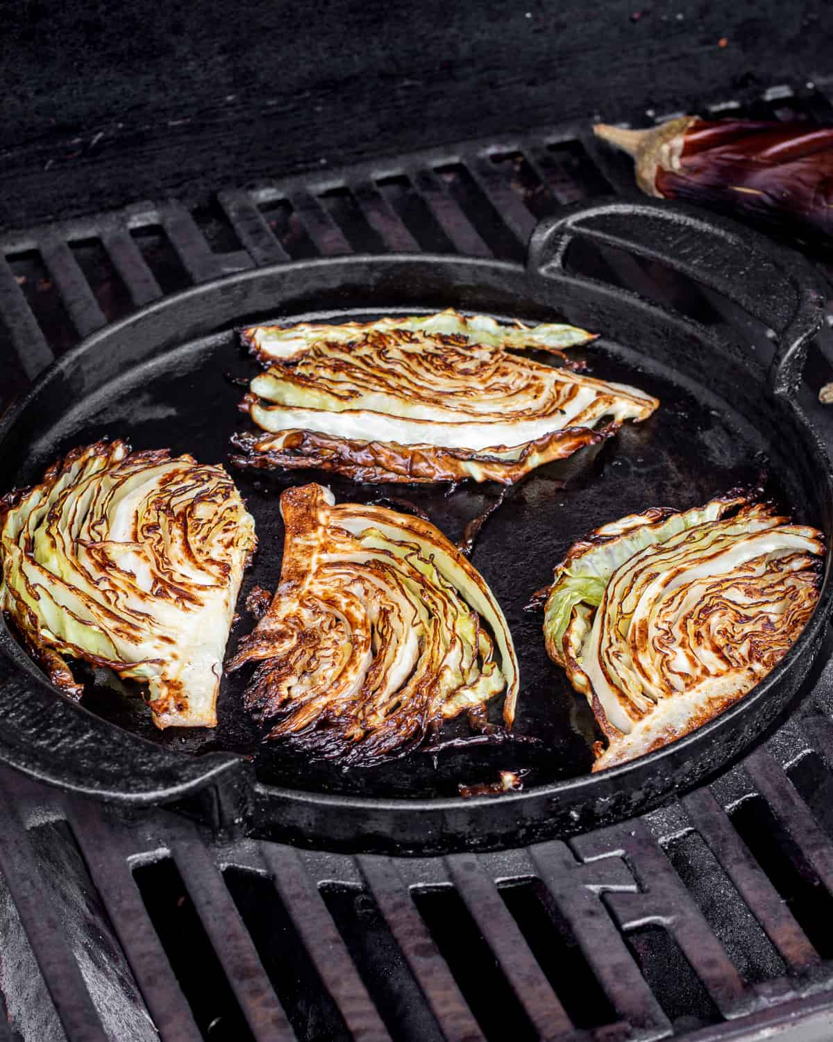 Charred cabbage wedges on the griddle of a gas grill.