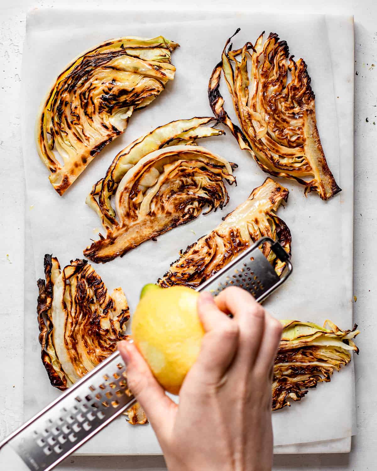 Hand zesting lemon over grilled cabbage wedges.