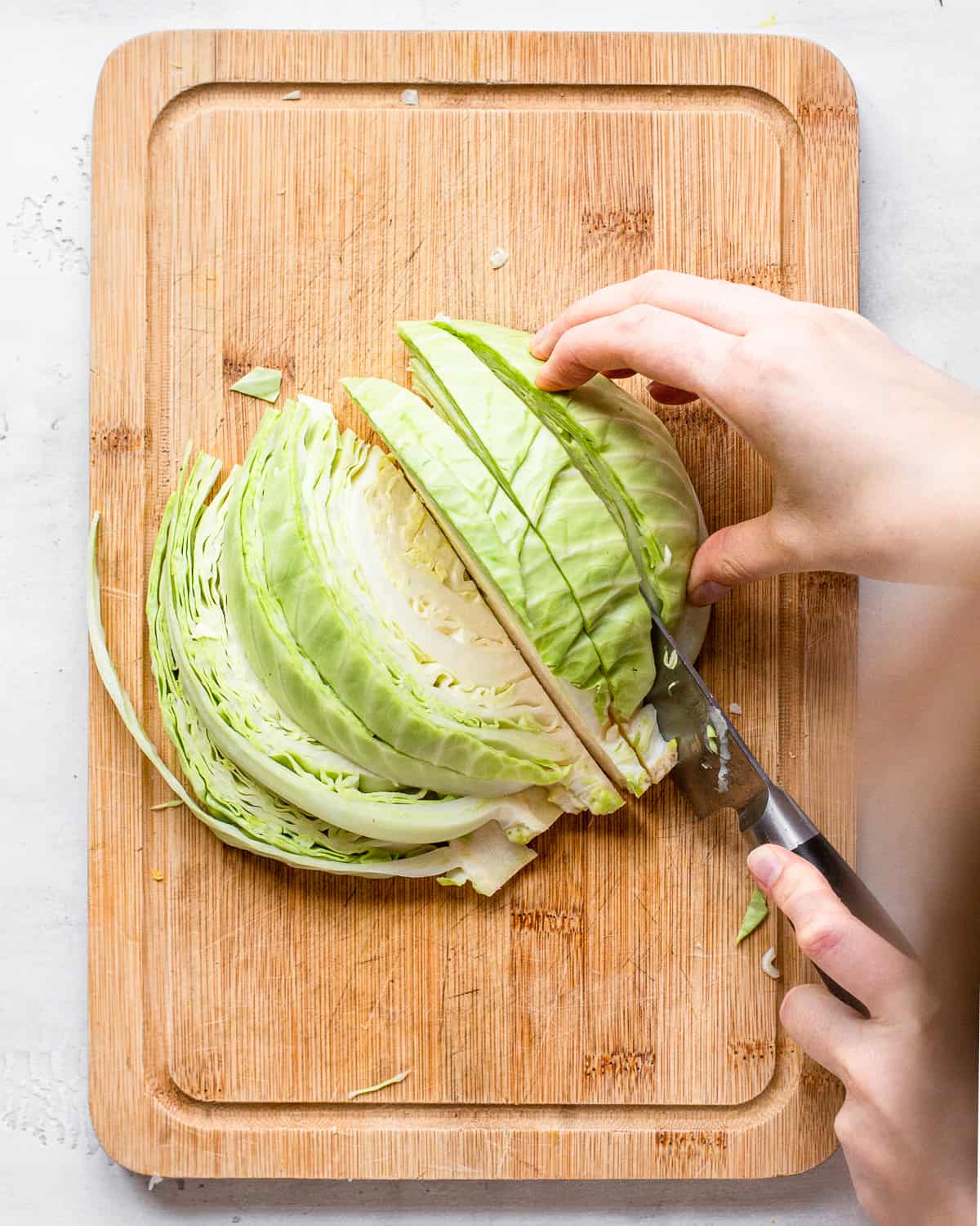 Hand slicing half a white cabbage into wedges on a wooden cutting board.