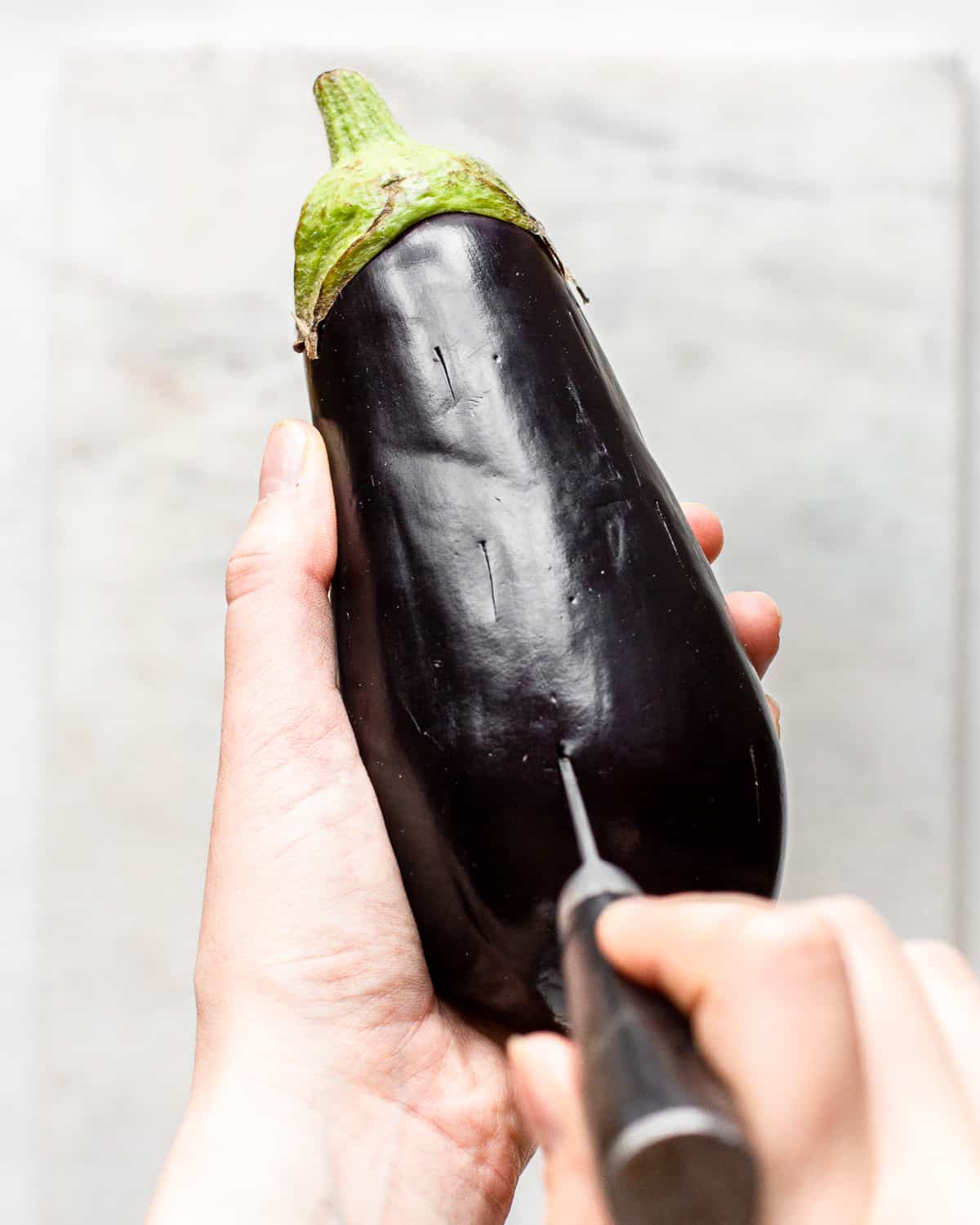 Hand poking holes into an eggplant with a small knife.
