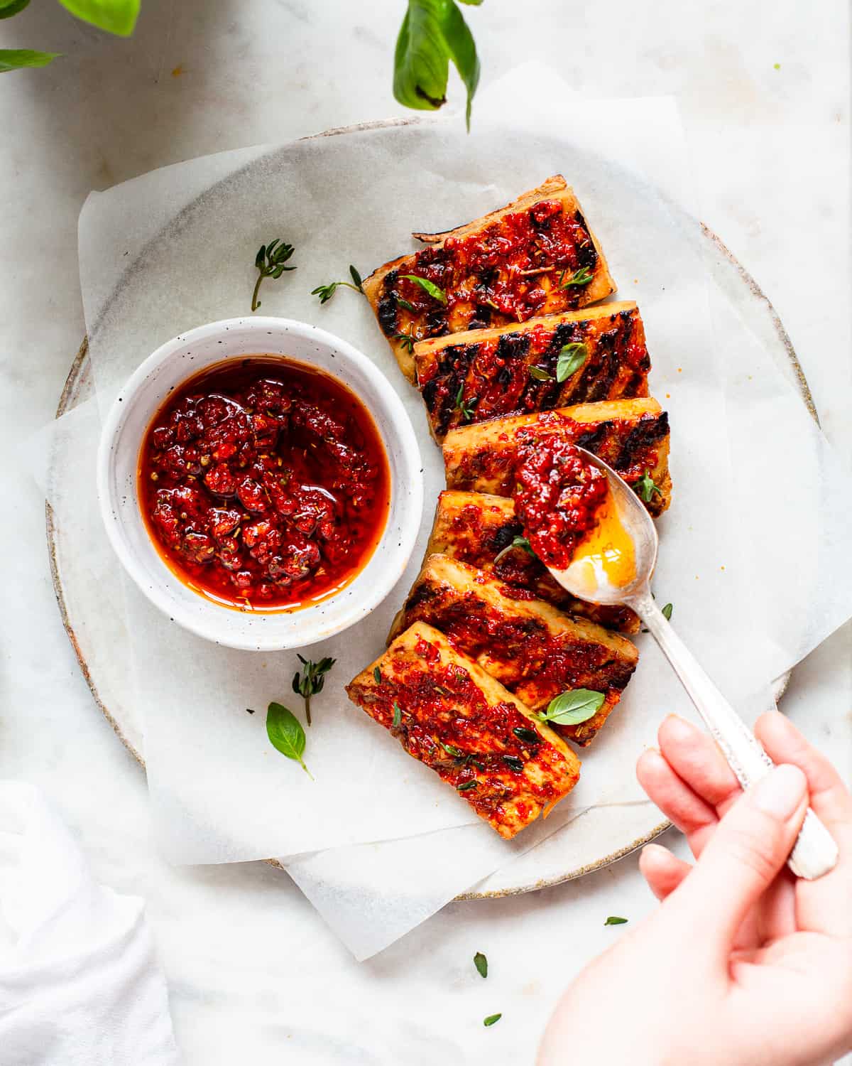 Hand adding a red harissa sauce onto tofu planks with a spoon.