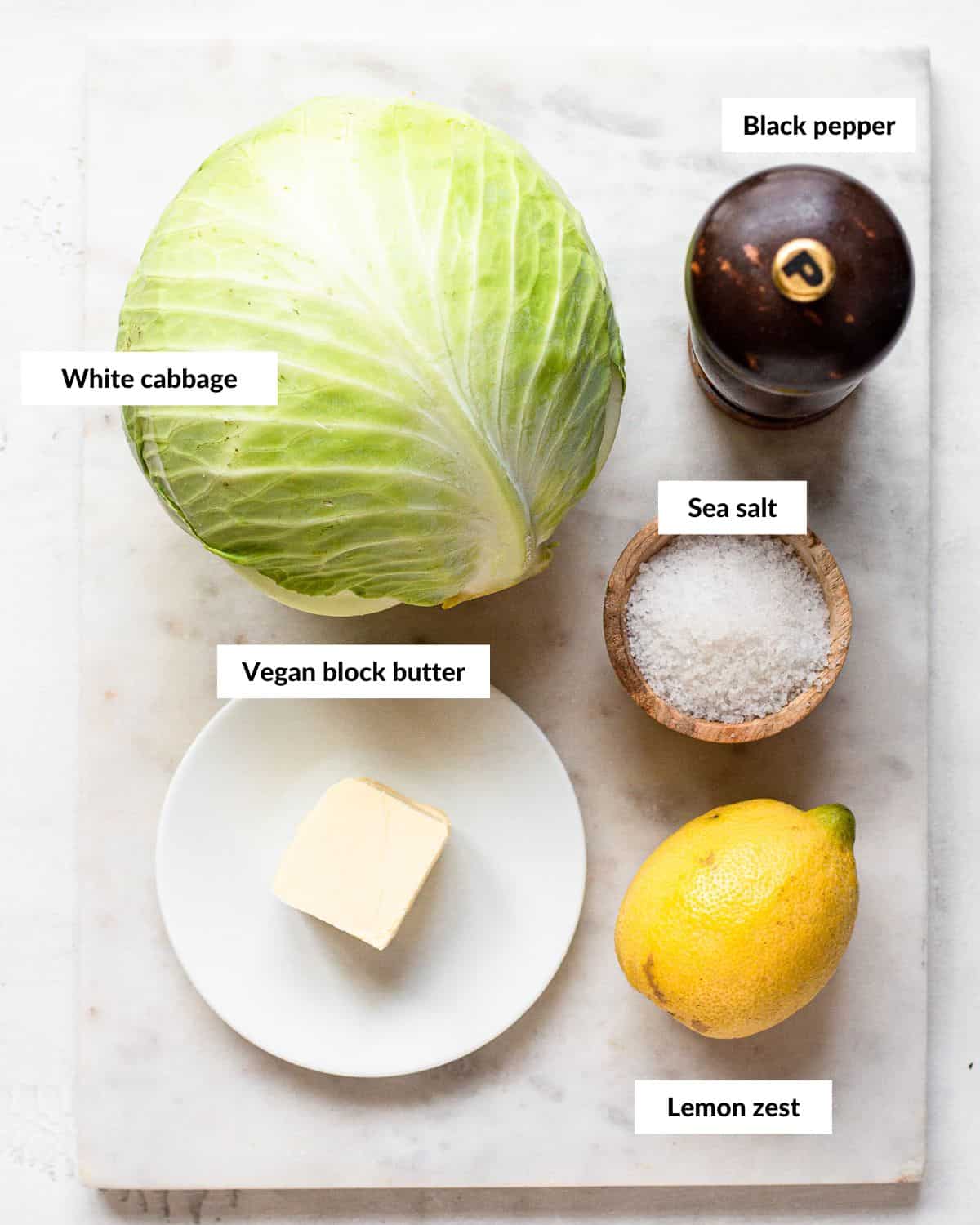 Ingredients for grilled cabbage with descriptive labels on a white marble platter.