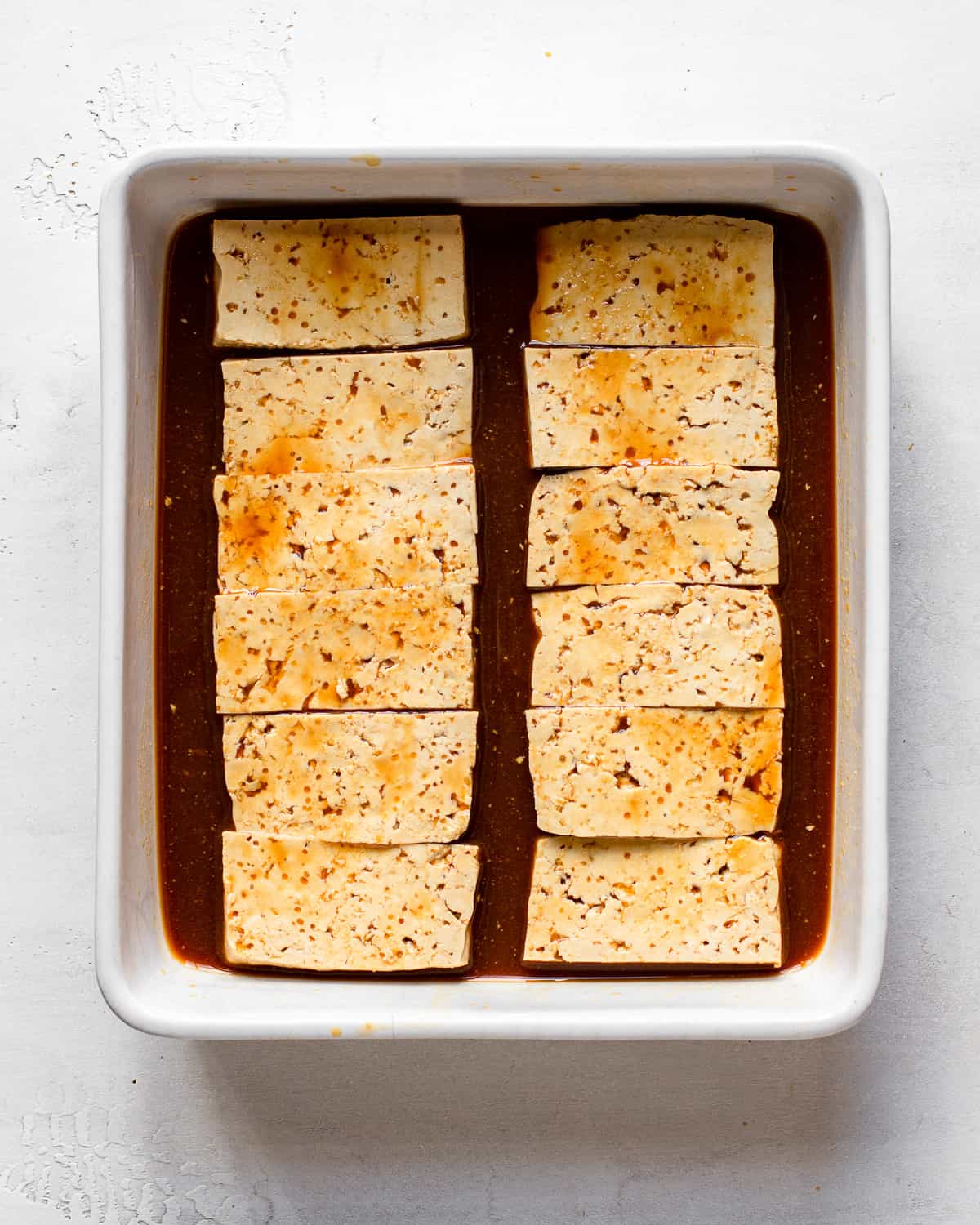 Twelve tofu planks marinating in a rectangular baking dish.