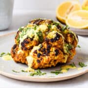 Grilled cauliflower head with charred areas, topped with a creamy yellow sauce, lemon zest, and fresh mint.