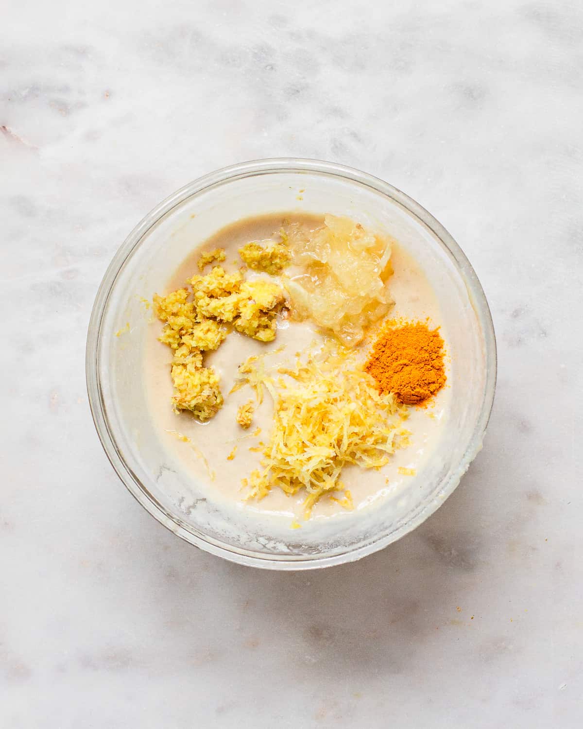 Small glass bowl with tahini, lemon zest, lemon pulp, grated ginger, and ground turmeric.