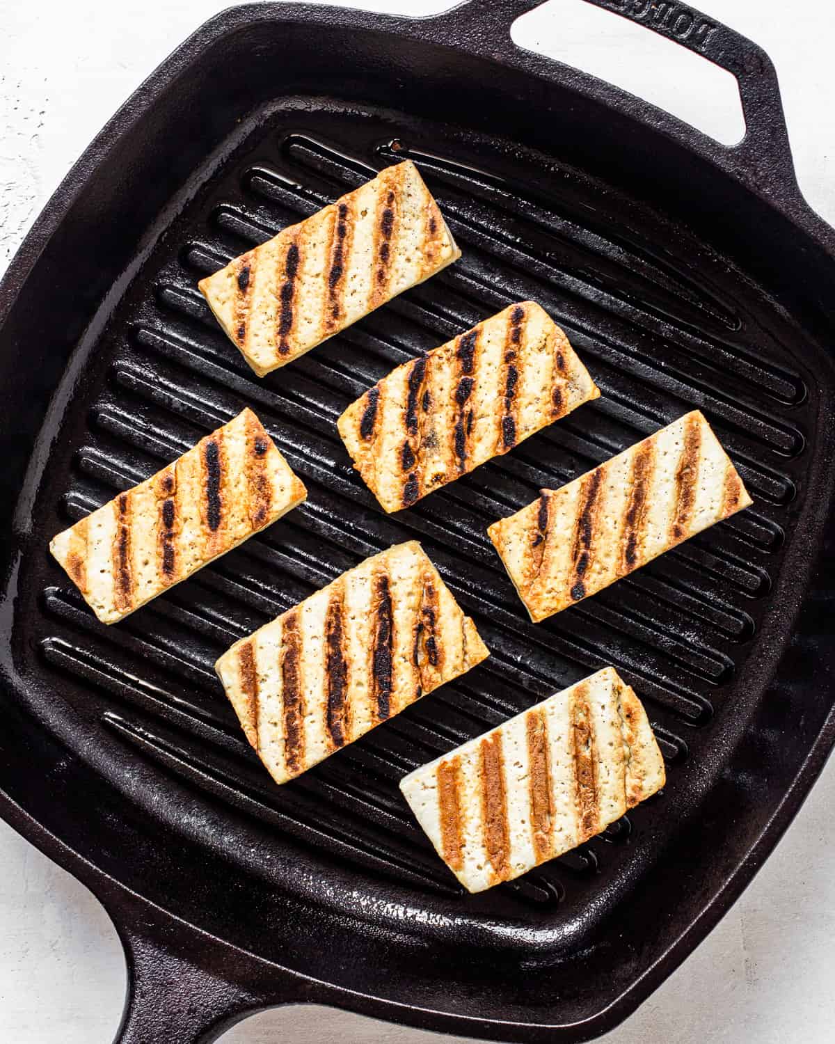 Six pieces of tofu with grill marks in a cast iron grill pan.