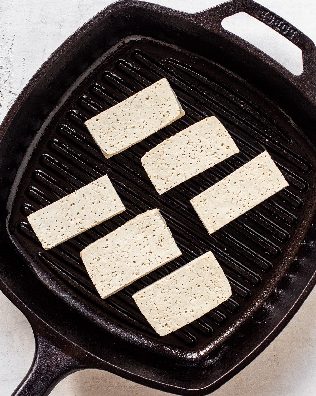 Six pieces of tofu in a greased cast iron grill pan.