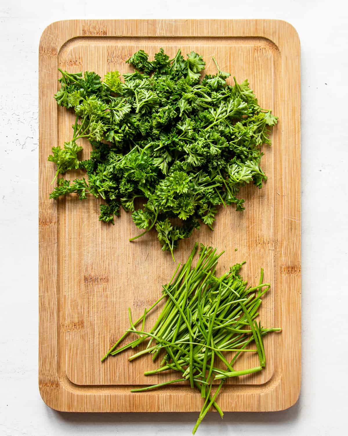 Parsley leaves and stems separated on a wooden cutting boards.