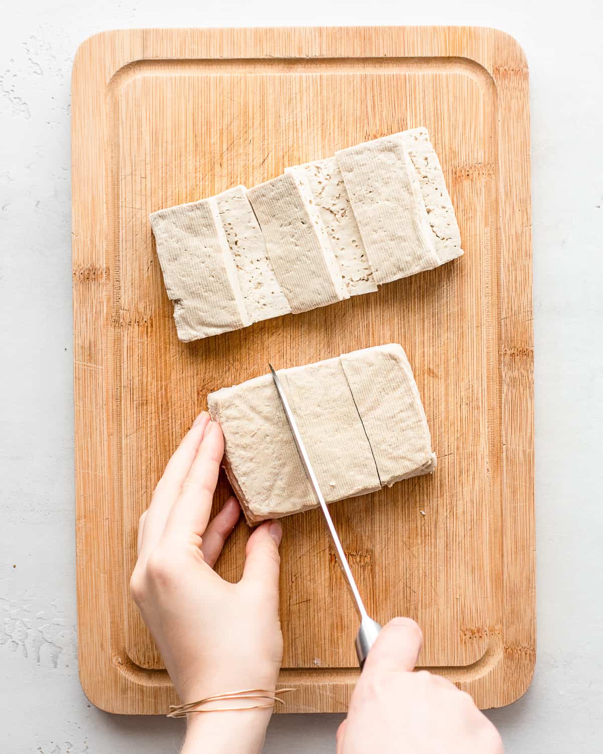 Hand cutting a tofu block into smaller tofu rectangles.