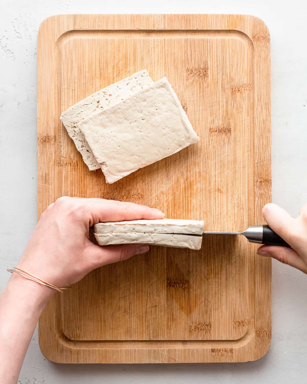 Hand cutting a tofu block lengthwise in half through the long edge.