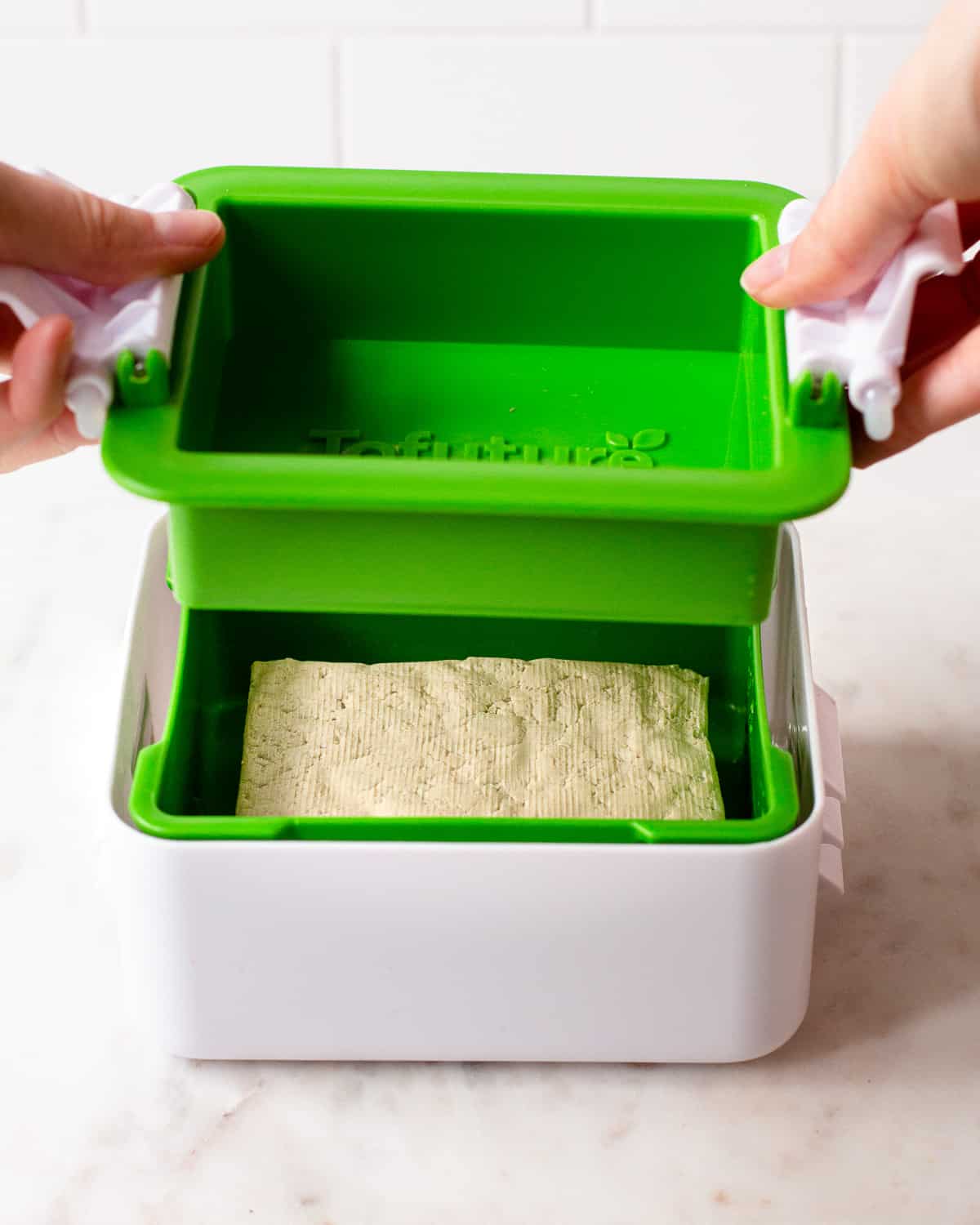 Hand closing a white and green plastic tofu press.