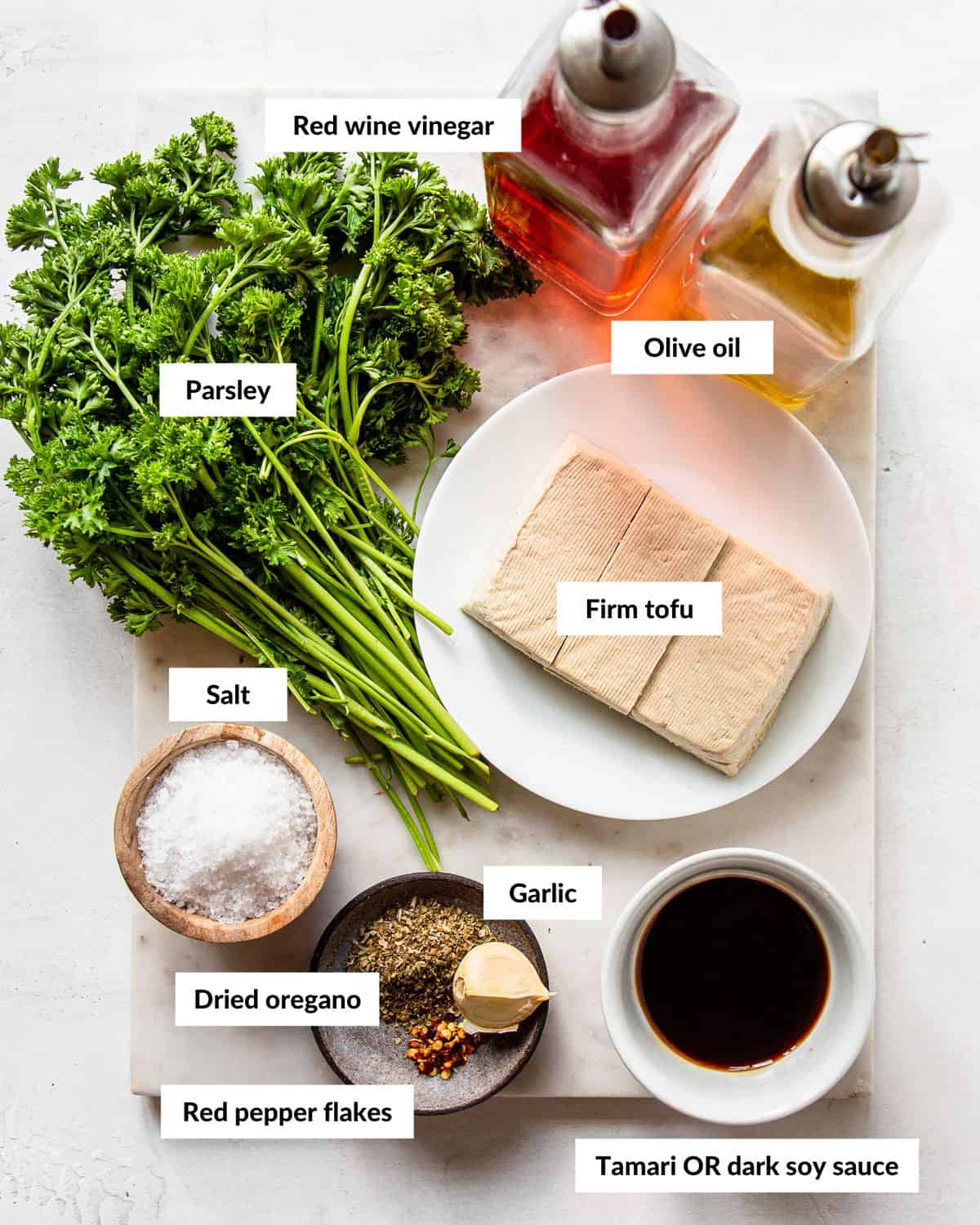 Ingredients for chimichurri tofu with descriptive labels on a white marble board.