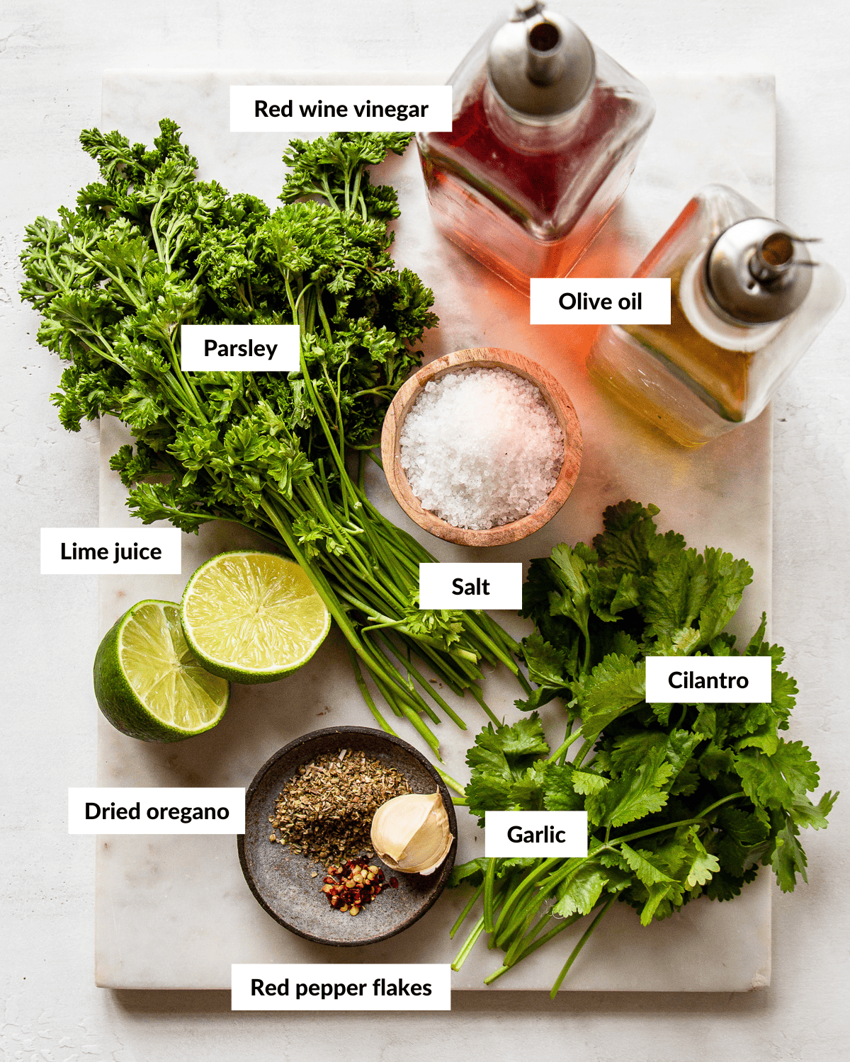 Ingredients for parsley cilantro chimichurri on a marble board with descriptive labels.