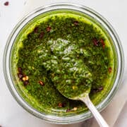 Bright green chimichurri in a glass bowl with an antique spoon.