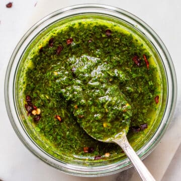 Bright green chimichurri in a glass bowl with an antique spoon.
