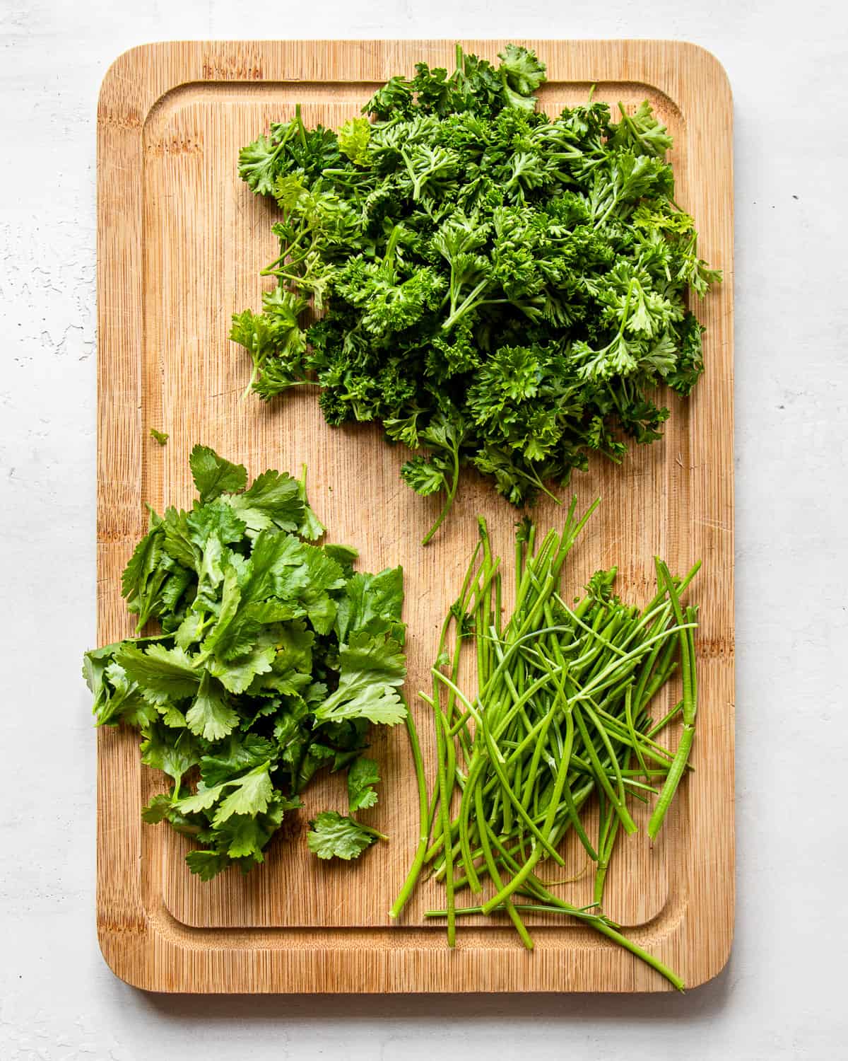 Parsley and cilantro with stems removed on a wooden cutting board.