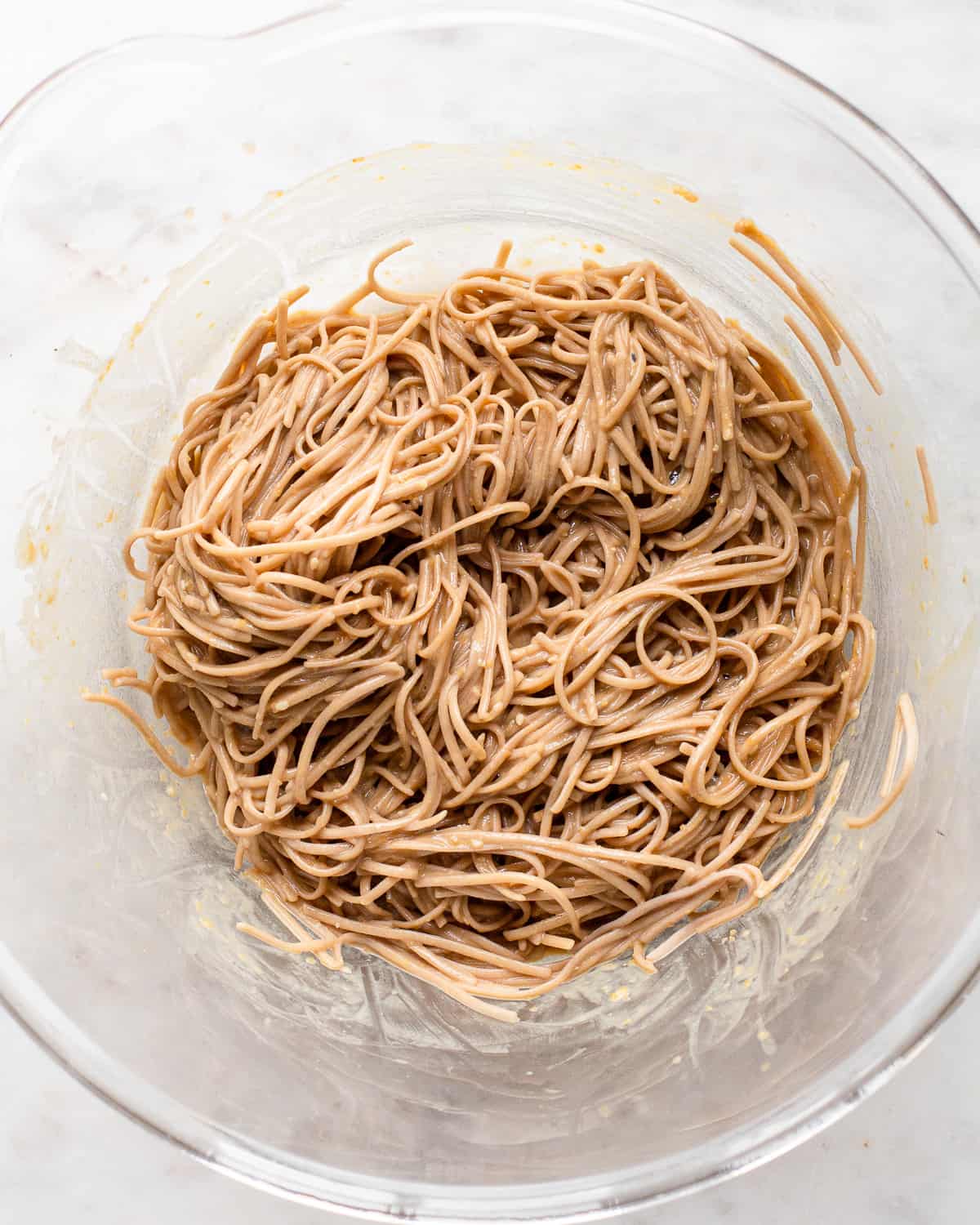 Soba noodles tossed in a tahini dressing in a glass salad bowl.