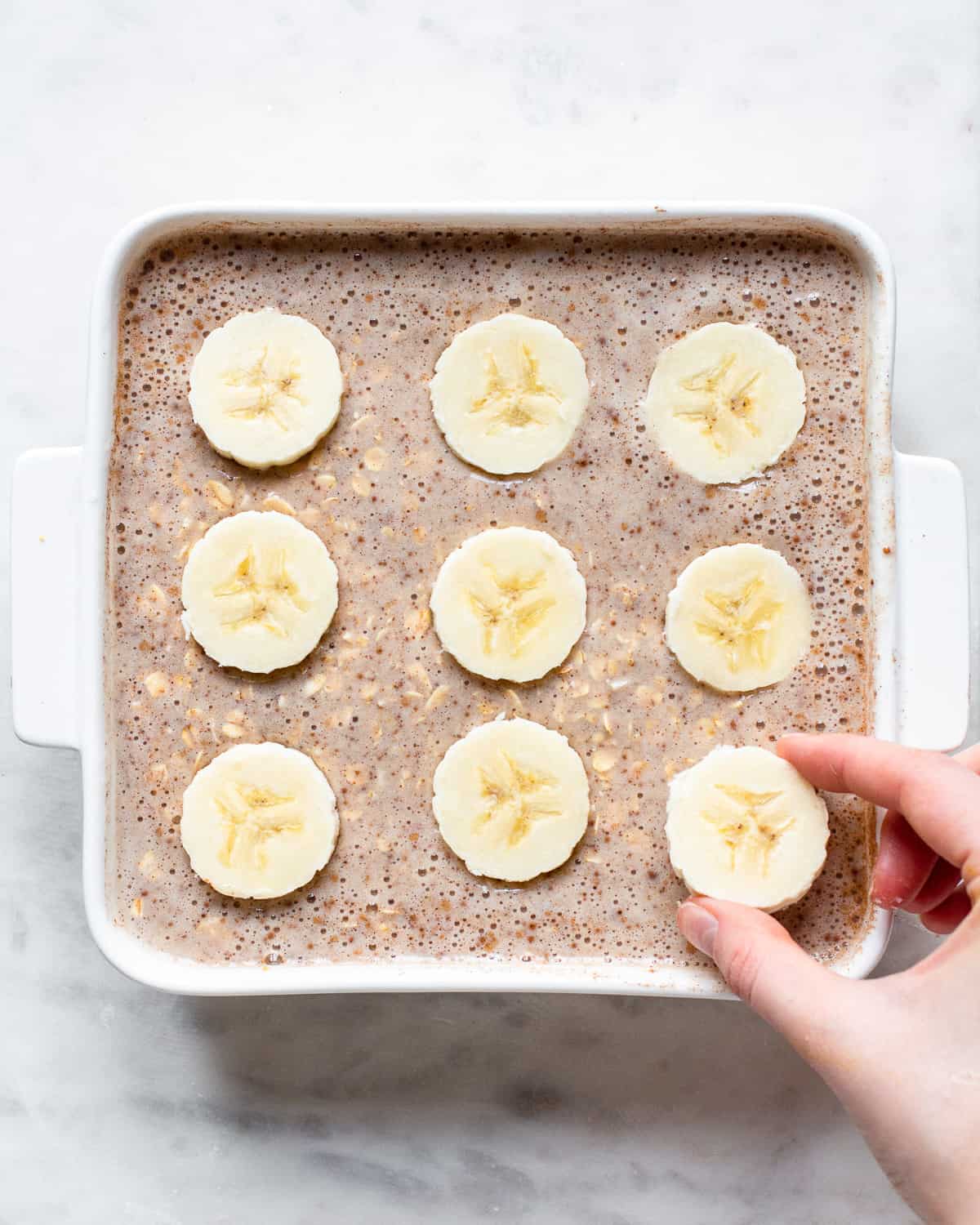 Unbaked oatmeal in a white baking dish topped with banana slices.