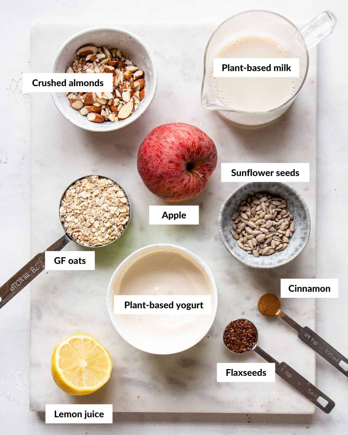 Bircher muesli ingredients on a white marble board with descriptive labels.