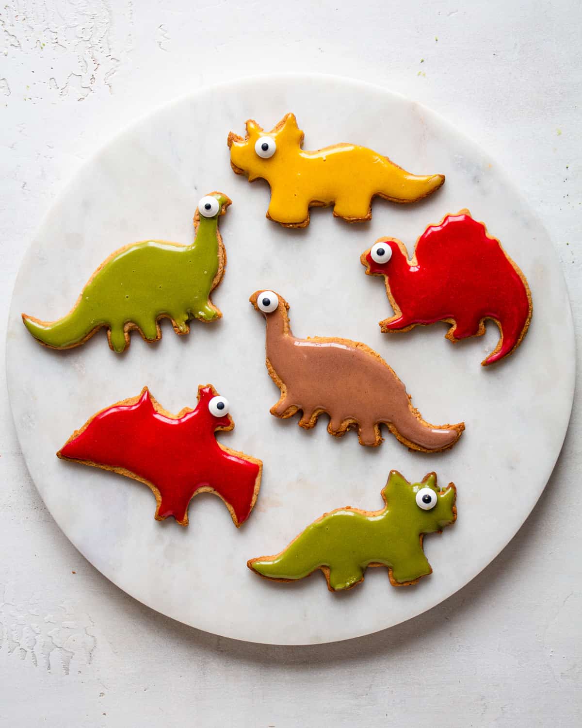 Dinosaur-shaped cookies with pink, green, yellow, and brown icing made from real foods.