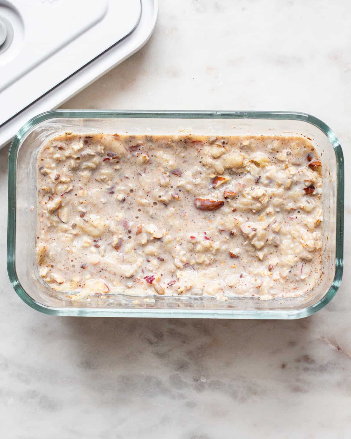 Bircher muesli in a glass container on a white marble board.
