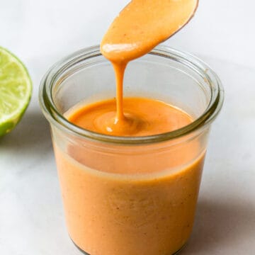 Bright orange poke bowl dressing dripping from a spoon into a glass Weck jar.