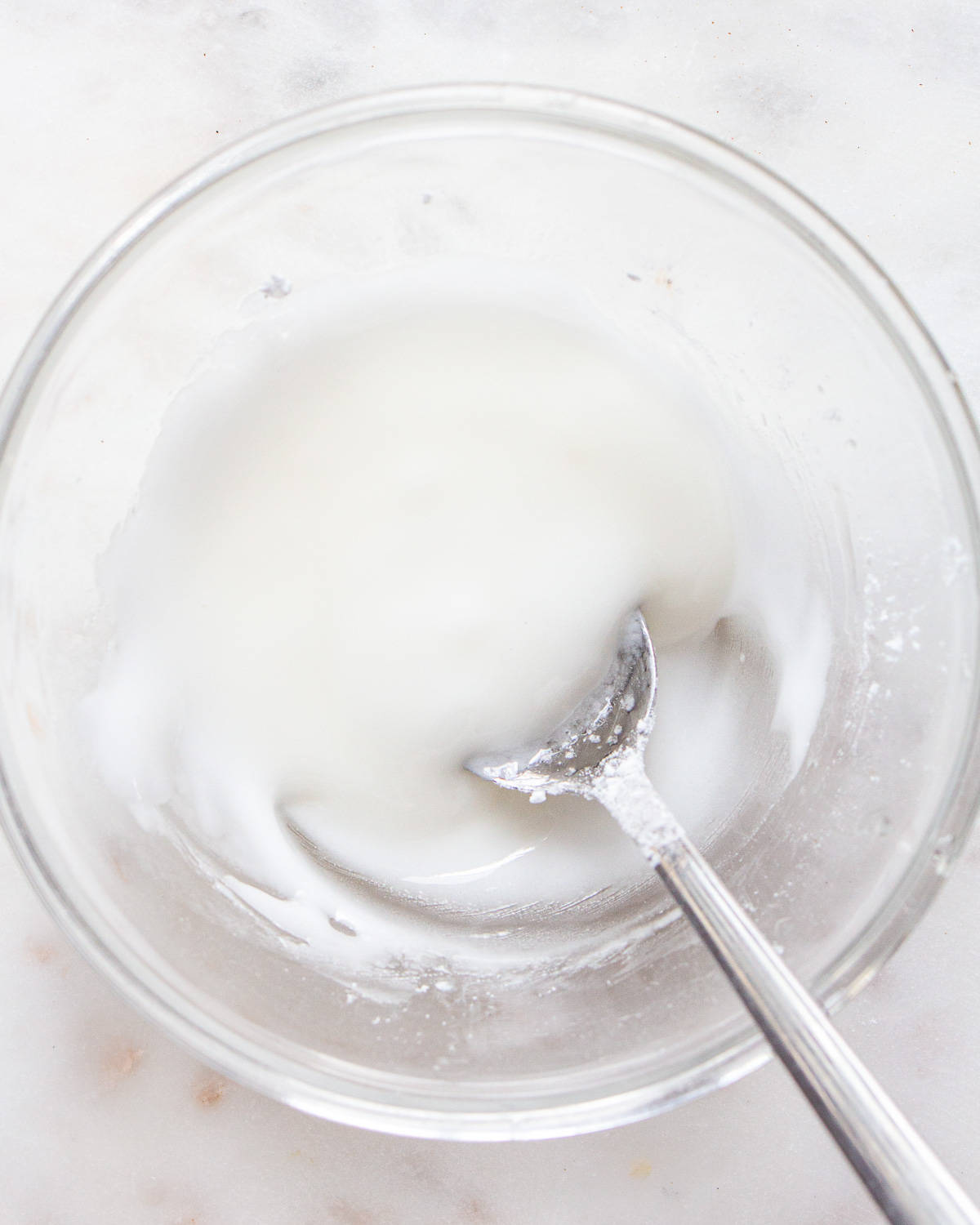 White icing in a small glass bowl with a spoon.