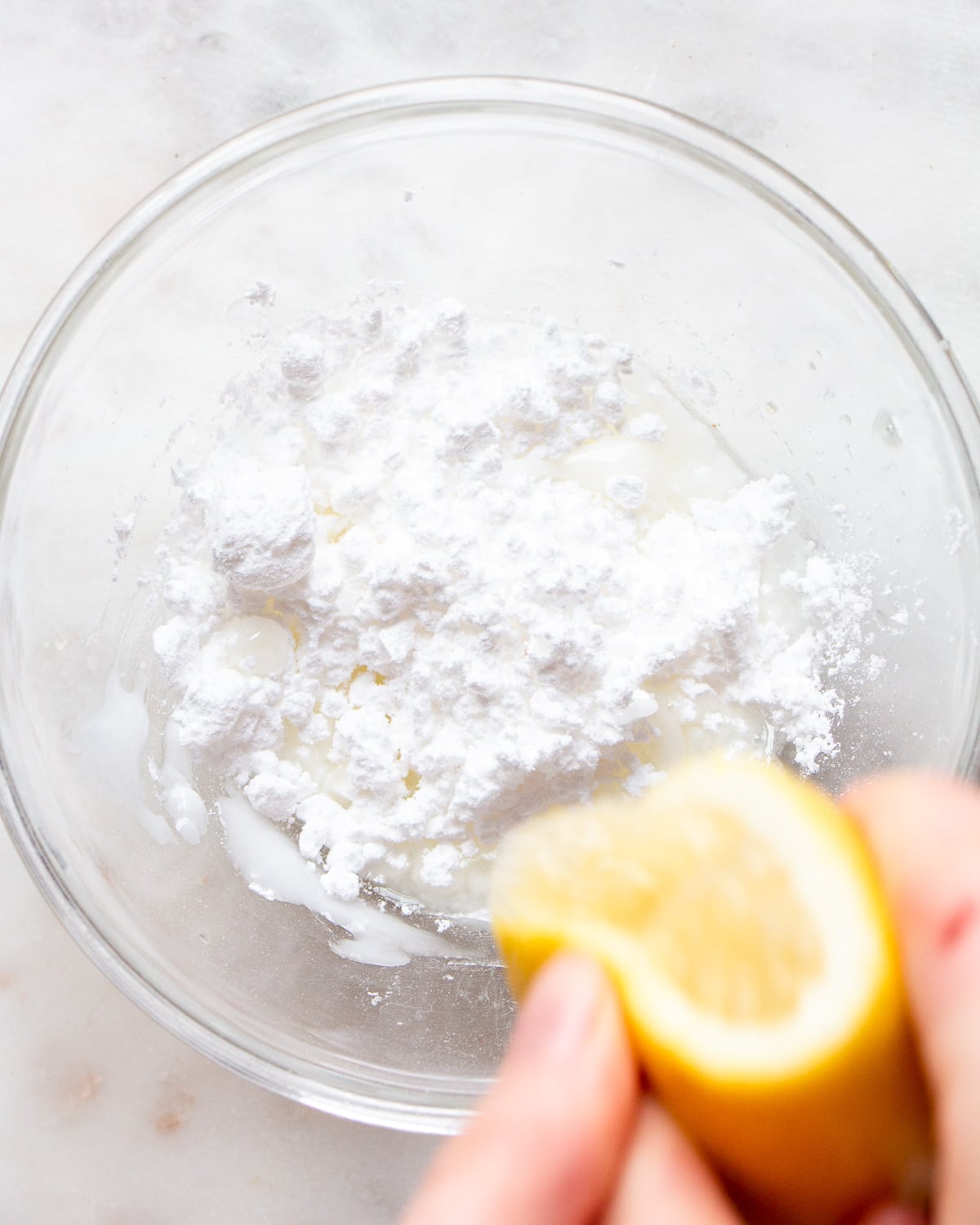 Hand squeezing lemon juice into a small bowl with icing sugar.