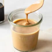 Balsamic tahini dressing dripping from a spoon into a jar.