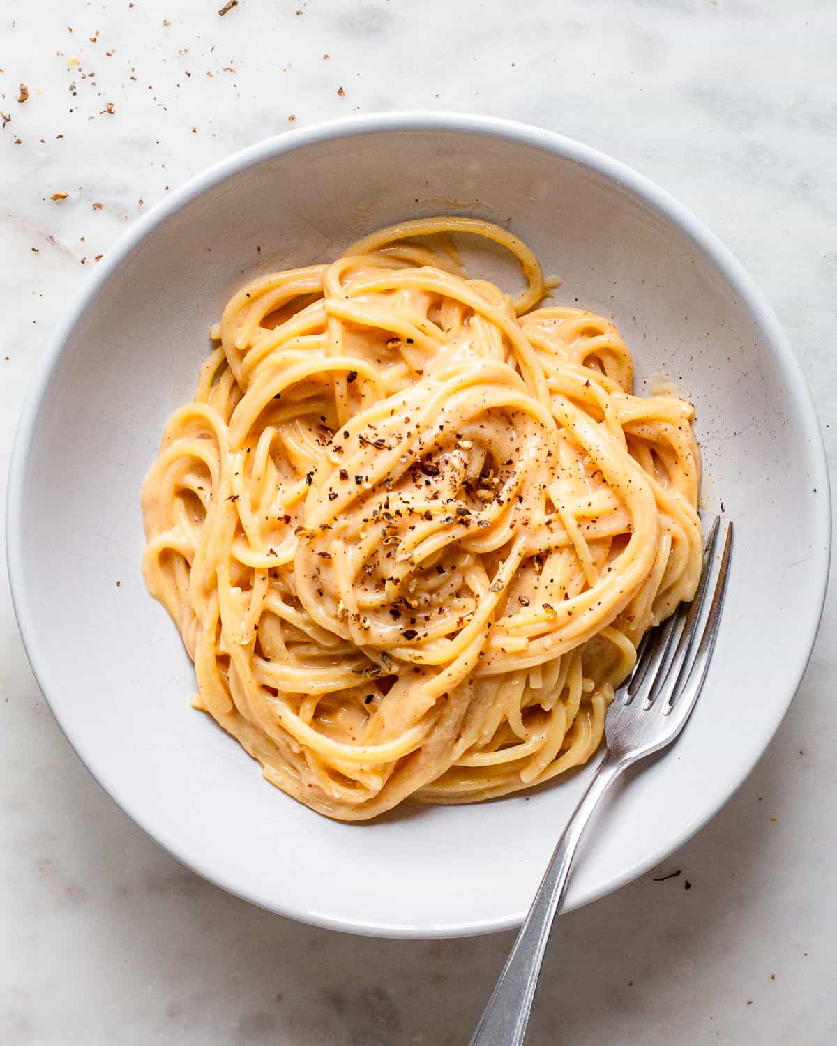 Cooked spaghetti tossed in a light orange sauce on a white ceramic plate.