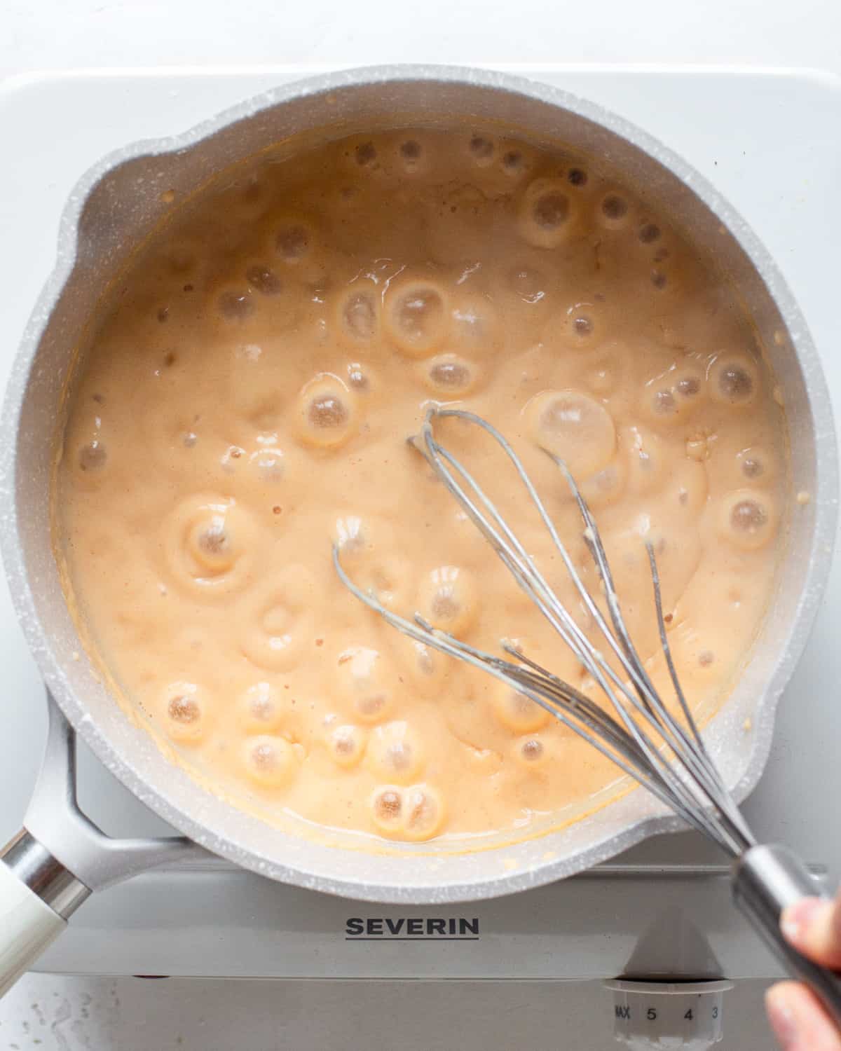 Simmering light orange sauce in a light grey saucepan.