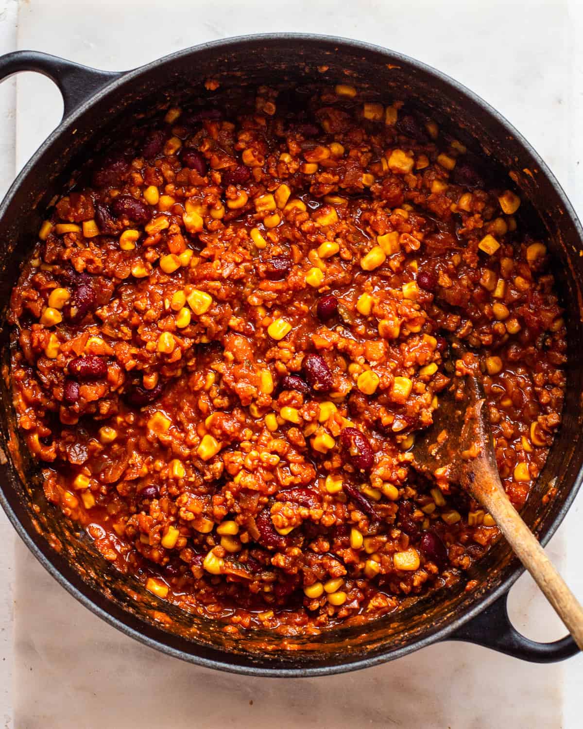 Finished vegan chili with soy crumbles, kidney beans, and corn in a black cast-iron pot.
