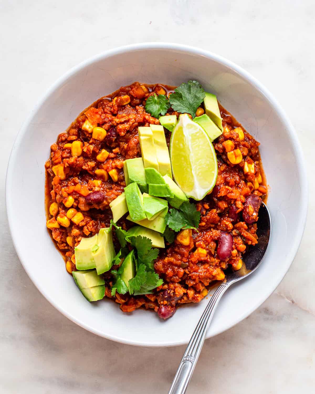 White ceramic bowl with vegan chili and topped with avocado.