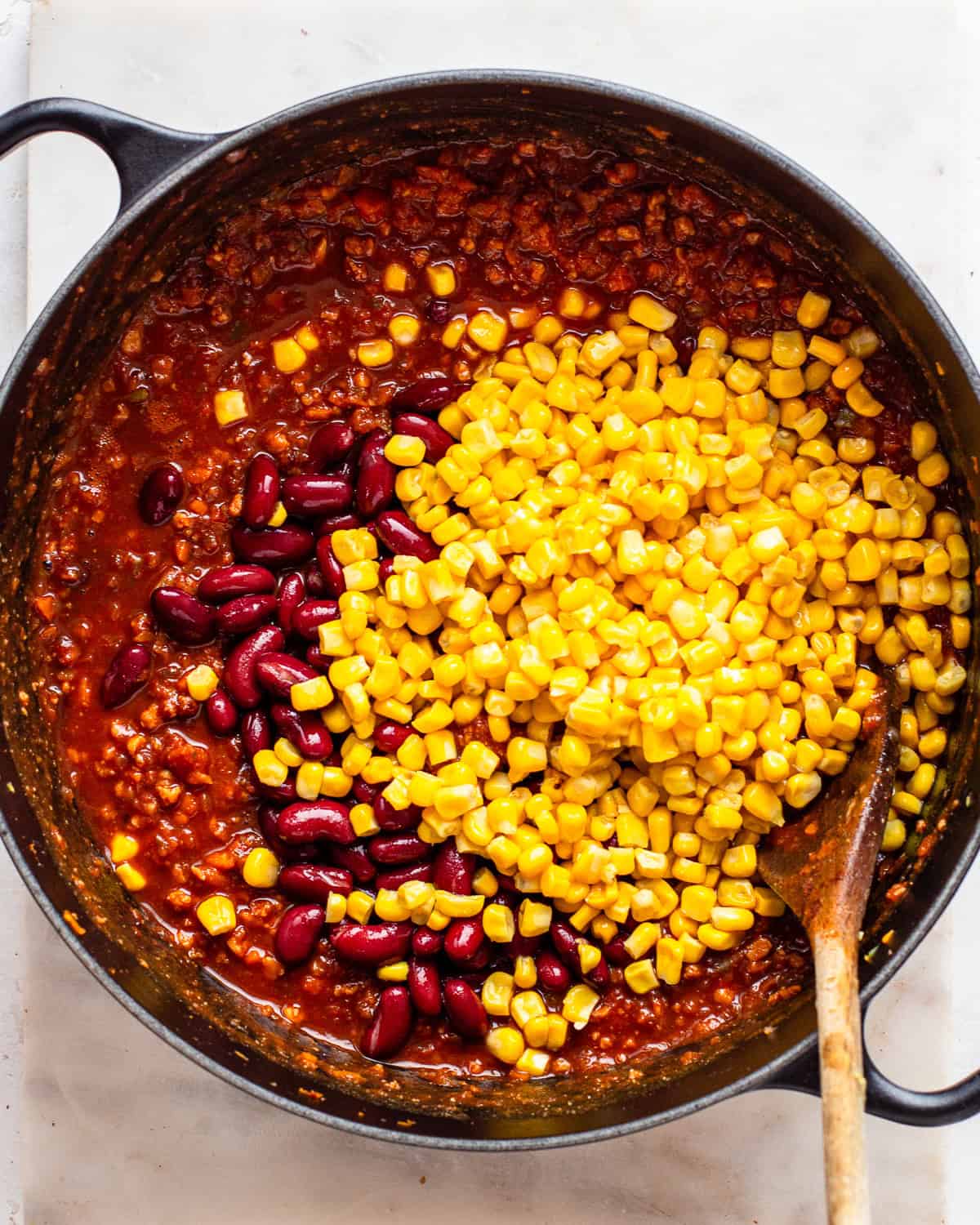Purple kidney beans and yellow corn in a large black pot with vegan chili.