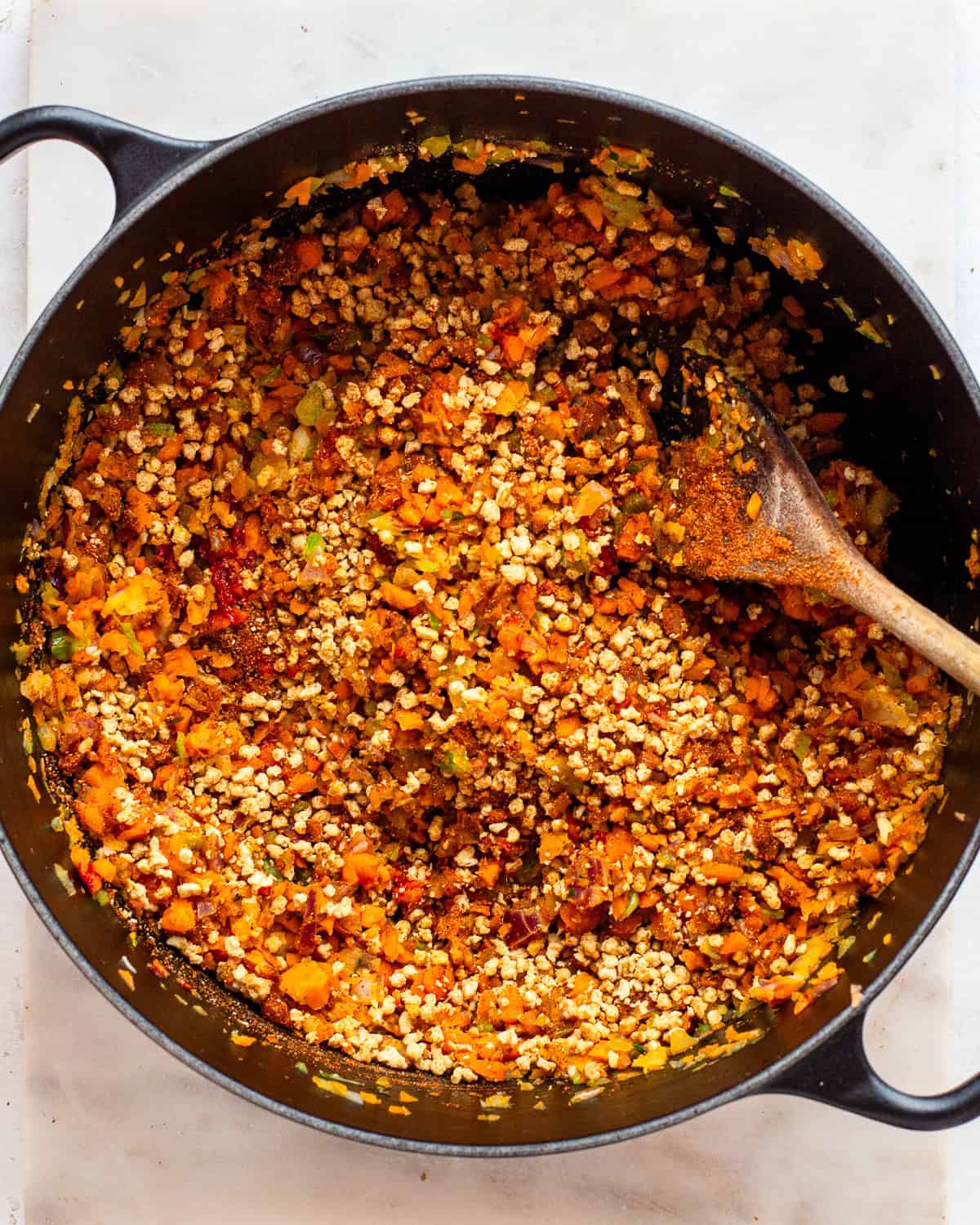 Fine soy crumbles and spices in a black pot with sautéed veggies.
