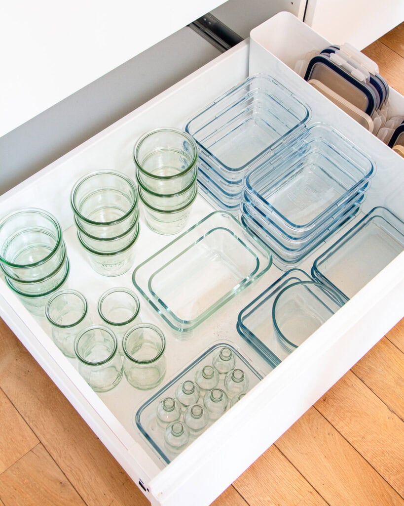 White kitchen drawer full of stackers glass containers of different shapes and sizes.