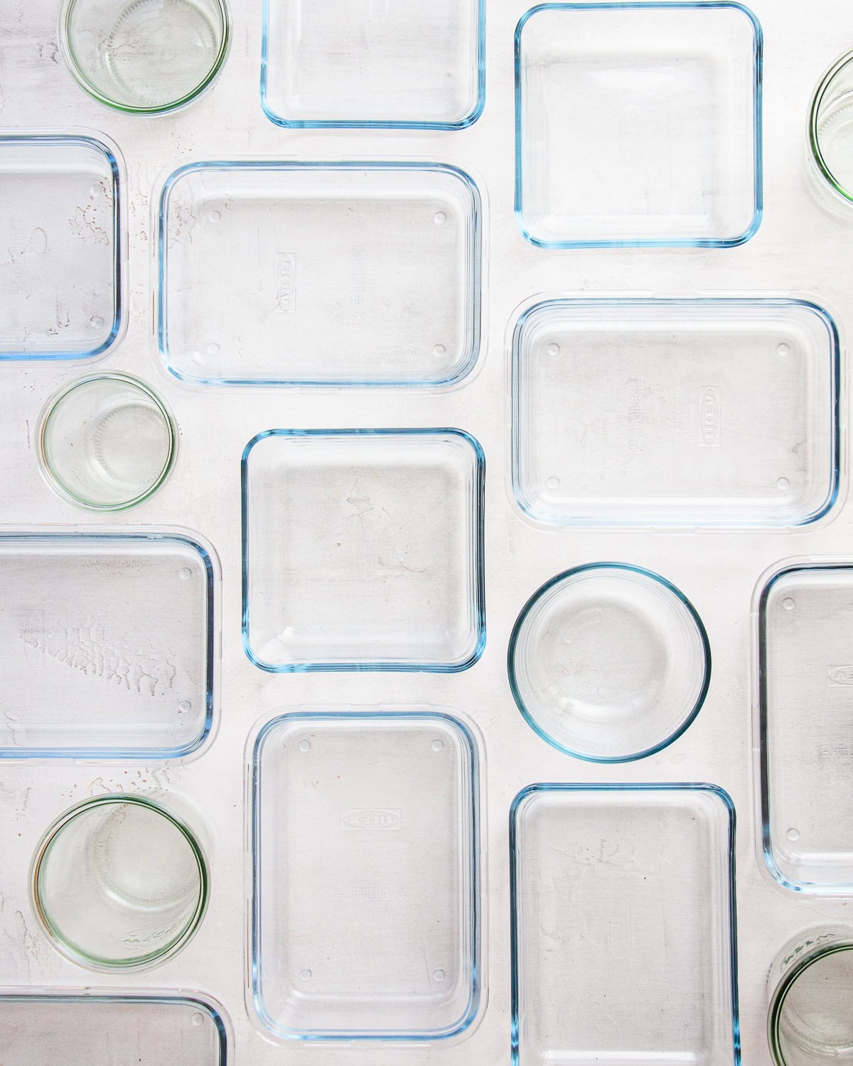 Glass food storage containers of different shapes without lids on a light grey backdrop.