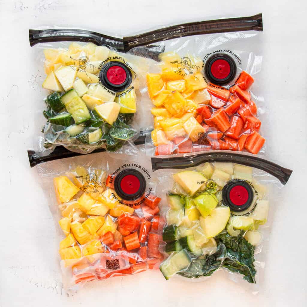 Four vacuum-seal plastic zip bags with pre-cut vegetables and citrus fruits inside.