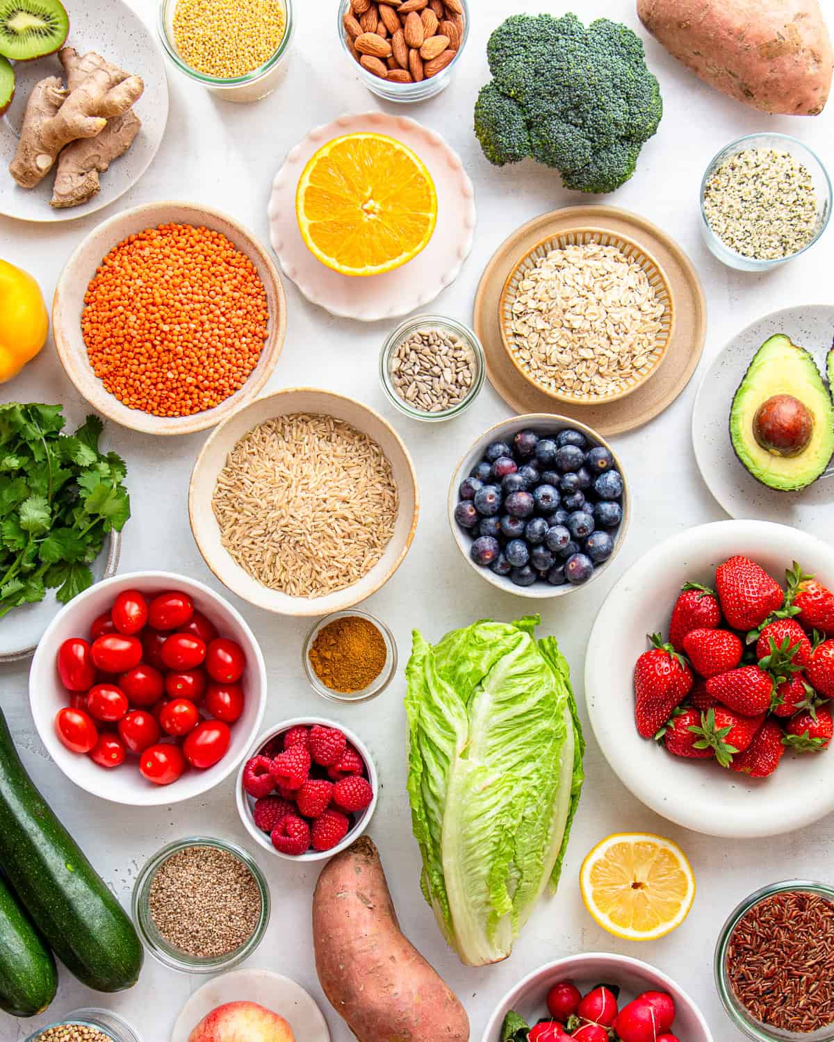 Lots of different fruits, veggies, nuts, and grains, on a light grey backdrop.