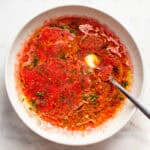 Olive oil swirled in tomato sauce in a beige ceramic bowl.